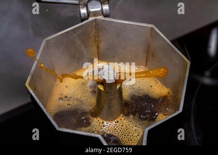 Flüssiger Kaffee kommt aus einer Kaffeekanne, die sich auf dem Herd in der Küche befindet. Kaffee mit Sahne in einer italienischen Moka-Kaffeemaschine Stockfoto