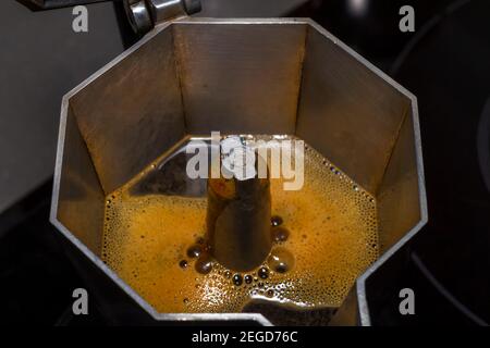 Flüssiger Kaffee kommt aus einer Kaffeekanne, die sich auf dem Herd in der Küche befindet. Kaffee mit Sahne in einer italienischen Moka-Kaffeemaschine Stockfoto