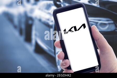 Galicia, Spanien; januar 09 2021: Hand hält ein Smartphone mit neuem KIA-Logo auf dem Bildschirm und verschwommene Autos auf dem Hintergrund. Speicherplatz kopieren Stockfoto