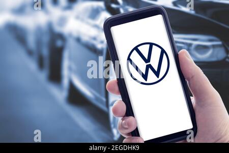 Galicia, Spanien; januar 09 2021: Hand hält ein Smartphone mit neuem Volkswagen-Logo auf dem Bildschirm und verschwommene Autos auf dem Hintergrund. Speicherplatz kopieren Stockfoto