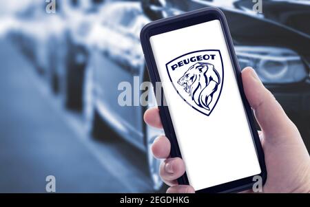 Galicia, Spanien; januar 09 2021: Hand hält ein Smartphone mit neuem PEUGEOT-Logo auf dem Bildschirm und verschwommene Autos auf dem Hintergrund. Speicherplatz kopieren Stockfoto