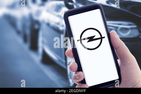 Galicia, Spanien; januar 09 2021: Hand hält ein Smartphone mit neuem OPEL-Logo auf dem Bildschirm und verschwommenen Autos auf dem Hintergrund. Speicherplatz kopieren Stockfoto