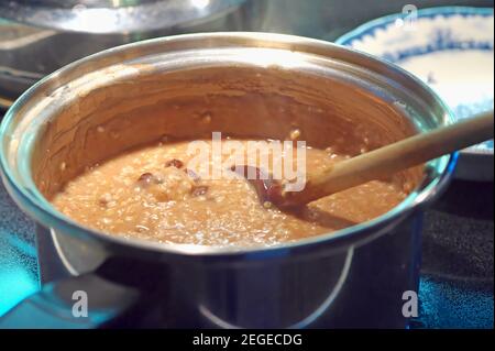 Gesundes Frühstückszerealien. Stahl-geschnittener Hafer mit Rosinen und einem Hauch Zimt Kochen in einem Edelstahltopf mit einem Holzlöffel. Stockfoto