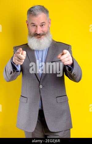 Studio Porträt reifen Geschäftsmann in grauen Anzug Punkte auf Kamera gekleidet, Ich wähle Sie Konzept, gelber Hintergrund Stockfoto