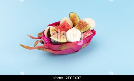 Exotischer Obstsalat aus geschnittenen Wassermelonen, Bananen und Feigen, serviert in einem halben Drachen auf blauem Hintergrund. Draufsicht. Stockfoto