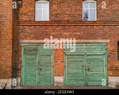 Zwei grüne Holztore zu Garagen im roten Backsteingebäude Stockfoto