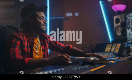Stilvoller Audio Engineer Producer, der im Music Recording Studio arbeitet, verwendet Mixing Board und Software, um modernen Hit Song zu erstellen. Black Artist Musiker Stockfoto