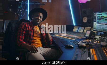 Stilvoller Audio Engineer, der im Music Recording Studio arbeitet, verwendet Mixing Board und Software, um einen modernen Hit zu kreieren. Blick auf Kamera Porträt von Stockfoto