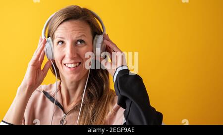 Porträt einer lächelnden jungen Frau mit Kopfhörern. Auf gelbem Hintergrund. Stockfoto