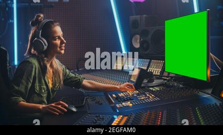 Stilvolle weibliche Audio-Engineer Producer arbeitet in Music Record Studio, verwendet Kopfhörer, Green Screen Computer Display, Mixer Board, Control Desk zu Stockfoto