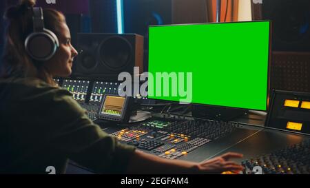 Stilvolle weibliche Audio-Engineer Producer arbeitet in Music Record Studio, verwendet Kopfhörer, Green Screen Computer Display, Mixer Board, Control Desk zu Stockfoto