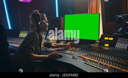 Stilvolle weibliche Audio-Engineer Producer arbeitet in Music Record Studio, verwendet Kopfhörer, Green Screen Computer Display, Mixer Board, Control Desk zu Stockfoto