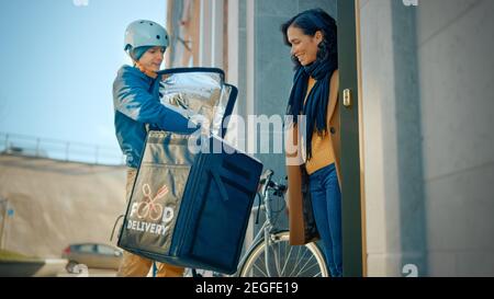 Happy Food Delivery Mann trägt Thermal Rucksack auf einem Fahrrad liefert Restaurant Bestellung an einen weiblichen Kunden. Courier liefert Takeaway Lunch an ein Mädchen Stockfoto