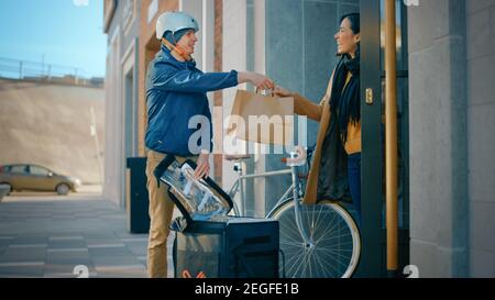 Happy Food Delivery Mann trägt thermischen Rucksack auf einem Fahrrad liefert Restaurant Bestellung an eine schöne weibliche Kunden. Kurier Liefert Takeaway Lunch Stockfoto