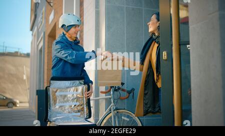 Happy Food Delivery Mann trägt Thermal Rucksack auf einem Fahrrad liefert Restaurant Bestellung an einen weiblichen Kunden. Courier liefert Takeaway Lunch nach Gorgeous Stockfoto