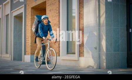 Handsome Happy Food Delivery Mann trägt Thermal Rucksack reitet sein Fahrrad durch die stilvolle moderne City District. Schuss lächelnder Courier Stockfoto