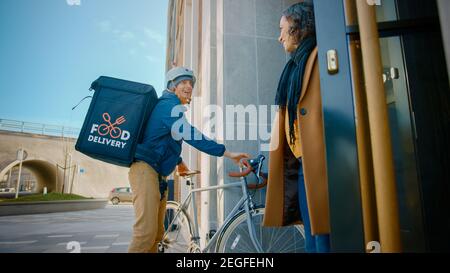 Happy Food Delivery Mann trägt thermischen Rucksack auf einem Fahrrad liefert Restaurant Bestellung an eine schöne weibliche Kunden. Kurier Liefert Takeaway Lunch Stockfoto