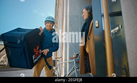 Happy Food Delivery Mann trägt thermischen Rucksack auf einem Fahrrad liefert Restaurant Bestellung an eine schöne weibliche Kunden. Kurier Liefert Takeaway Lunch Stockfoto