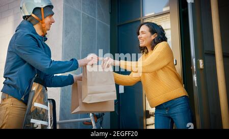 Happy Food Delivery Mann auf dem Fahrrad liefert Restaurant Bestellung an schöne weibliche Kunden. Courier liefert Takeaway Lunch zu Gorgeous Girl in Modern Stockfoto