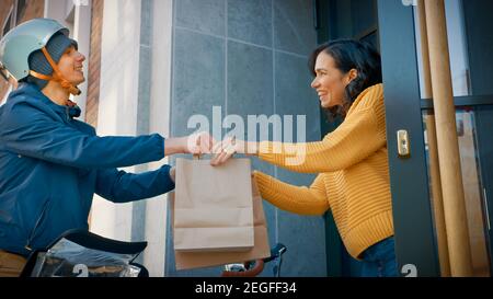 Happy Food Delivery man on a Bike liefert Restaurant Order an eine schöne Kundin. Courier liefert Takeaway Lunch zu Gorgeous Girl in Modern Stockfoto
