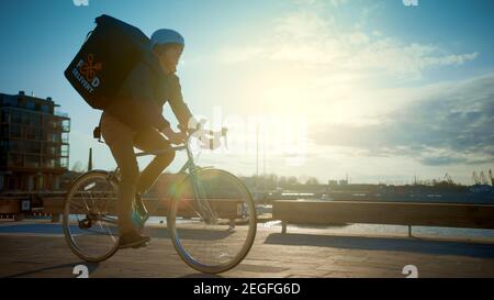 Happy Food Delivery Kurier Tragen Thermal Rucksack fährt ein Fahrrad auf der Straße, um Bestellungen und Pakete für Kunden zu liefern. Sonniger Tag in der Stadt mit Stockfoto