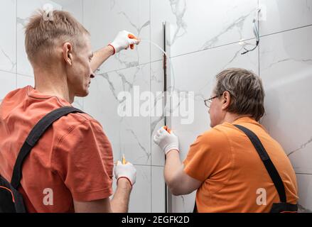 Arbeiter installieren eine Silikondichtung im Metallprofil der Duschabtrennung. Stockfoto