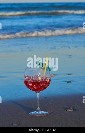 Ein köstlicher und erfrischender Cocktail auf dem Sand des Strandes in der Nähe der Wellen. Stockfoto