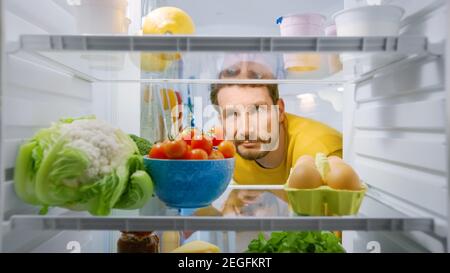 Innenküche Kühlschrank: Junger enttäuschter Mann schaut in den Kühlschrank. Der Mann fand nichts für seine Snack-Zeit. Blickwinkel POV Aufnahme aus dem Kühlschrank Stockfoto