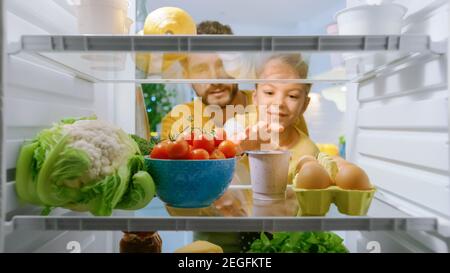 Kamera im Inneren Küche Kühlschrank: Papa Lifts nette kleine Tochter zu wählen, was sie will, um aus dem Kühlschrank zu nehmen, wählt sie gesunde Joghurt. Punkt Stockfoto