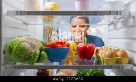 Schöne junge Frau schaut in den Kühlschrank und nimmt Gemüse. Frau Bereitet Gesunde Mahlzeit Mit Lebensmittel. Blickwinkel POV von innen nach Stockfoto