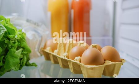 Shot aus der Küche Kühlschrank: Box Pack von Eiern, frischen Säften und grünem Gemüse. Point of View POV Aufnahme aus Kühlschrank voller Gesundheit Stockfoto