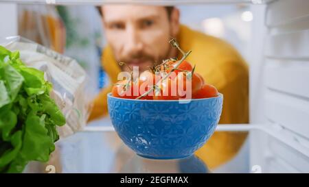 Kamera in der Küche Kühlschrank: Handsome man öffnet Kühlschranktür, denkt, Schüssel mit Tomaten nehmen. Mann, Der Eine Gesunde Mahlzeit Zubereitet. Blickwinkel POV Aufnahme aus Stockfoto