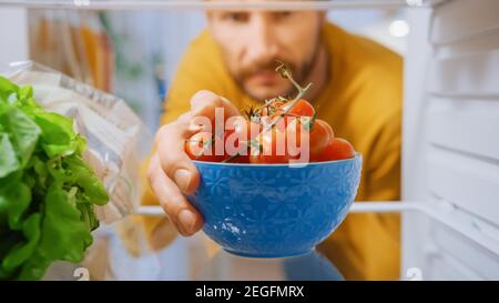 Kamera in der Küche Kühlschrank: Handsome man öffnet Kühlschranktür, nimmt Schüssel mit Tomaten. Mann, Der Eine Gesunde Mahlzeit Zubereitet. Blickwinkel POV Aufnahme aus Stockfoto