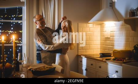 Ältere Paare in der Liebe haben romantischen Abend, Tanzen in der Küche, Jubiläum feiern. Romantischer Abend mit Wein, Festtisch in stilvoller Atmosphäre Stockfoto