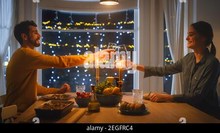 Happy Young Couple in Love Haben romantisches Abendessen, Toasten einander mit Gläsern Wein, Essen leckeres Essen in der Küche, feiern, reden Stockfoto