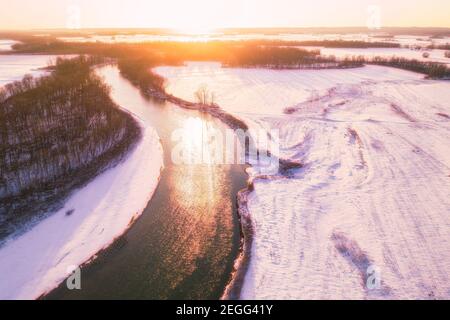 Eine Sonnenuntergangsszene über dem weißen Fluss in Jackson County, IN. Der Schnee hat einen magentafarbenen Farbton und mehrere Schwärme von Sandhügelkranen sind auf dem Fluss und in der Luft. Stockfoto