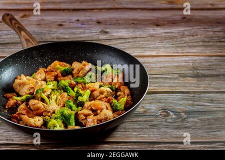 Würziges Hähnchenteriyaki mit Brokkoli in Pfanne auf rustikalem Holzhintergrund. Stockfoto