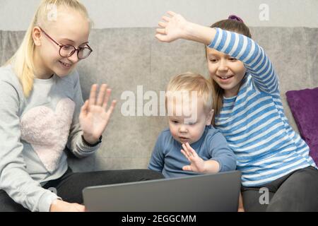 Zwei Schwestern und ein kleiner Bruder sprechen auf dem Laptop auf dem Sofa. Hohe Qualität Stockfoto