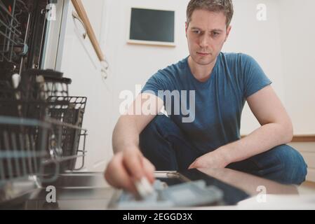 Mann, der Waschmitteltablett in die Spülmaschine legte. Stockfoto