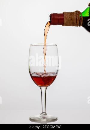 Gießt Rotwein in klares Glas auf weißem Hintergrund. Stockfoto