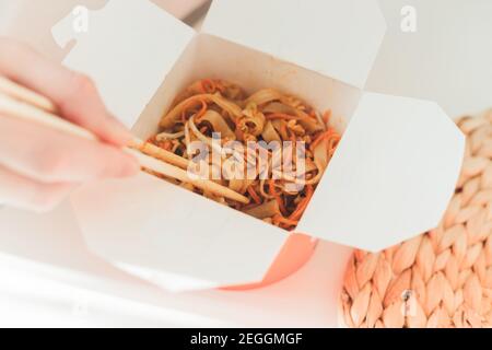 Wok-Nudeln in der Take-away-Box. Frau beim Essen mit Essstäbchen, Nahaufnahme auf weiblichen Händen. Traditionelle chinesische Küche mit Gemüse und Meeresfrüchten. Stockfoto