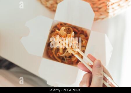 Wok-Nudeln in der Take-away-Box. Frau beim Essen mit Essstäbchen, Nahaufnahme auf weiblichen Händen. Traditionelle chinesische Küche mit Gemüse und Meeresfrüchten. Stockfoto