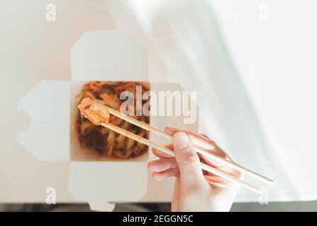 Wok-Nudeln in der Take-away-Box. Frau beim Essen mit Essstäbchen, Nahaufnahme auf weiblichen Händen. Traditionelle chinesische Küche mit Gemüse und Meeresfrüchten. Stockfoto