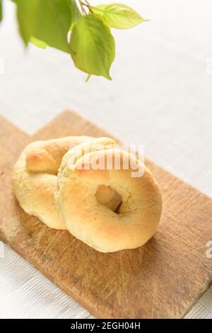 Taralli ist ein traditionelles italienisches Snack-Essen, typisch für die regionale Küche Apuliens. Hausgemachte süße Tarallini ist aus Holz Cutten Board mit Feder Zweig Stockfoto