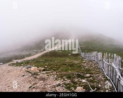 Blick von Cairnwell in Richtung Càrn Aosda inmitten des Glenshee Ski Centers, zwischen den Wolken, die die Schneetäune zeigen, um den Schnee zu treiben. Stockfoto