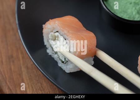 Eine Lachs-Sushi-Rolle mit Essstäbchen halten Stockfoto
