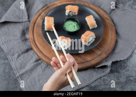 Eine Lachs-Sushi-Rolle mit Essstäbchen halten Stockfoto