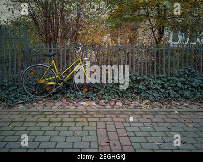 Altes gelbes Fahrrad, das sich gegen den Metallzaun lehnt Stockfoto