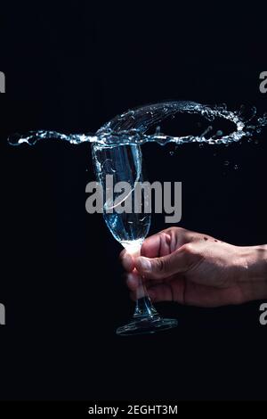 Blick auf einen Glaskelz gefüllt mit Wasser geschüttelt Hand mit schwarzem Hintergrund Stockfoto