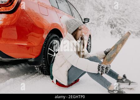 Eine junge Frau sitzt bei einem roten Auto und hält eine Karte in ihren Händen. Reisekonzept. Stockfoto